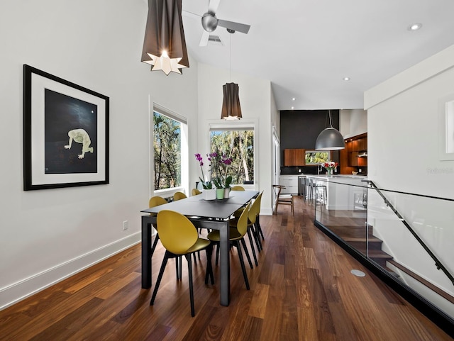 dining space with dark wood-style floors, visible vents, a high ceiling, and baseboards