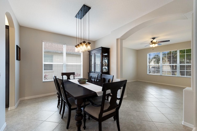 dining area with ceiling fan with notable chandelier, arched walkways, baseboards, and light tile patterned floors