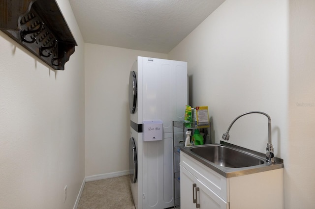 laundry room featuring a textured ceiling, light tile patterned floors, stacked washer and dryer, a sink, and cabinet space