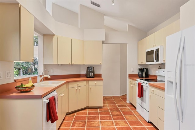 kitchen with white appliances, a sink, visible vents, vaulted ceiling, and cream cabinetry