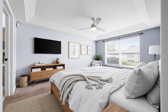 carpeted bedroom featuring a tray ceiling, ceiling fan, and a textured ceiling