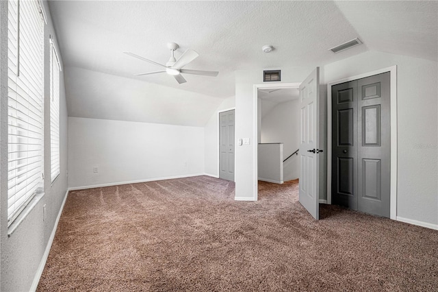 unfurnished bedroom featuring a textured ceiling, vaulted ceiling, carpet, and visible vents