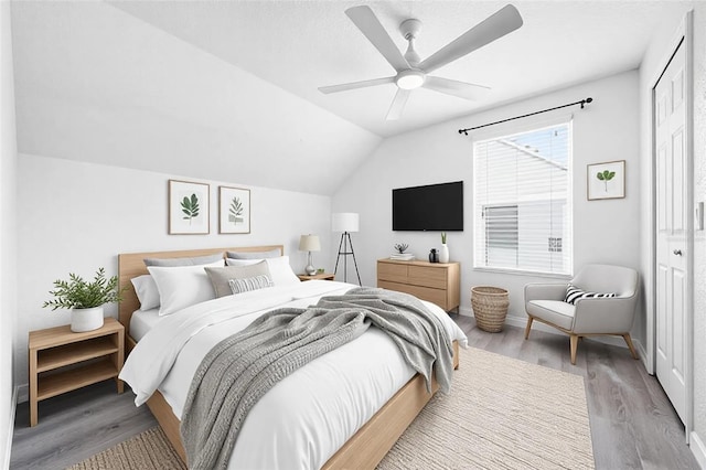 bedroom featuring lofted ceiling, a closet, a ceiling fan, wood finished floors, and baseboards