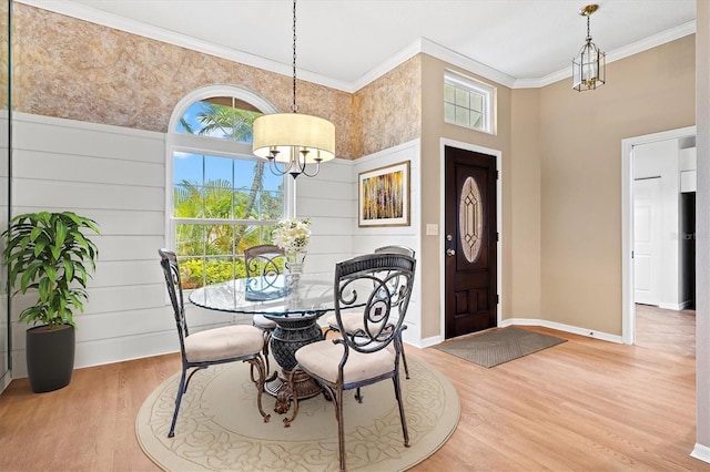 dining space with a notable chandelier, a high ceiling, wood finished floors, baseboards, and crown molding