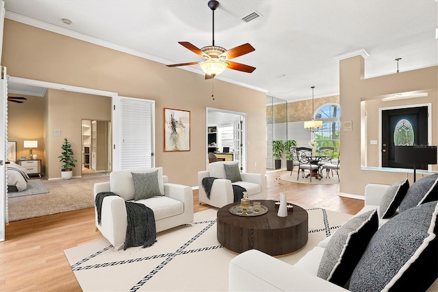 living room featuring a ceiling fan, wood finished floors, visible vents, and crown molding