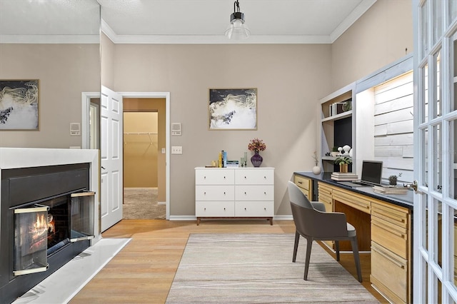 office area featuring ornamental molding, a glass covered fireplace, light wood-style floors, and baseboards