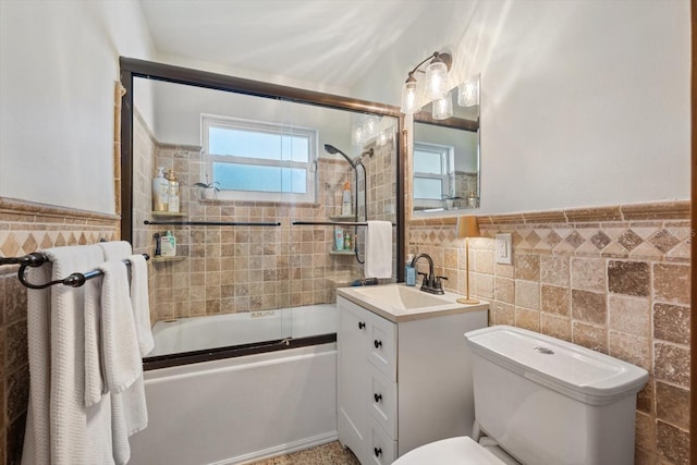 full bathroom featuring toilet, bath / shower combo with glass door, vanity, tile walls, and wainscoting