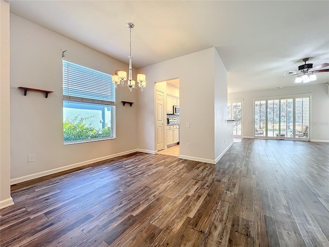 unfurnished room with dark wood-style flooring, baseboards, and ceiling fan with notable chandelier