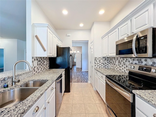 kitchen featuring light tile patterned floors, stainless steel appliances, tasteful backsplash, white cabinets, and a sink