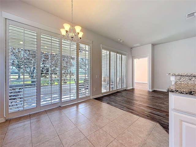 unfurnished dining area with baseboards, visible vents, a chandelier, and light tile patterned flooring