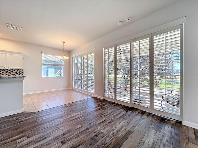 unfurnished dining area with a chandelier, visible vents, dark wood finished floors, and baseboards