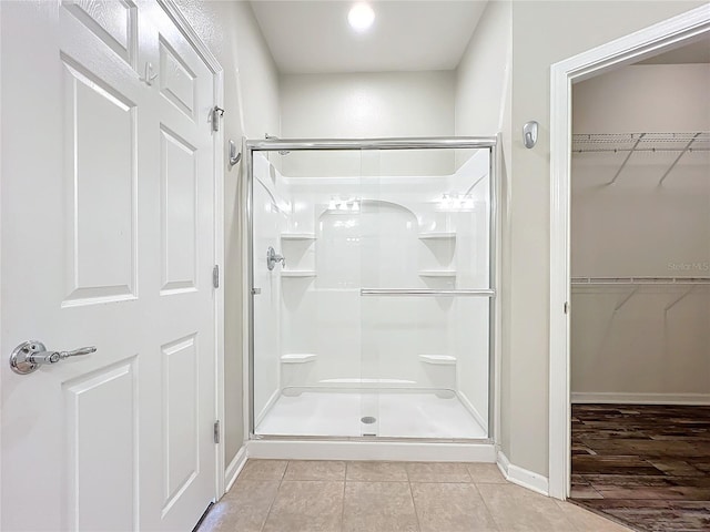 bathroom with baseboards, a spacious closet, a shower stall, and tile patterned floors