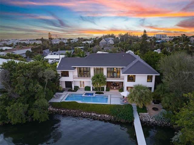 back of property at dusk featuring a balcony, an outdoor pool, a hot tub, a tile roof, and a patio area