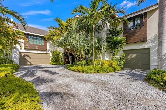 view of front of home with gravel driveway, an attached garage, and stucco siding