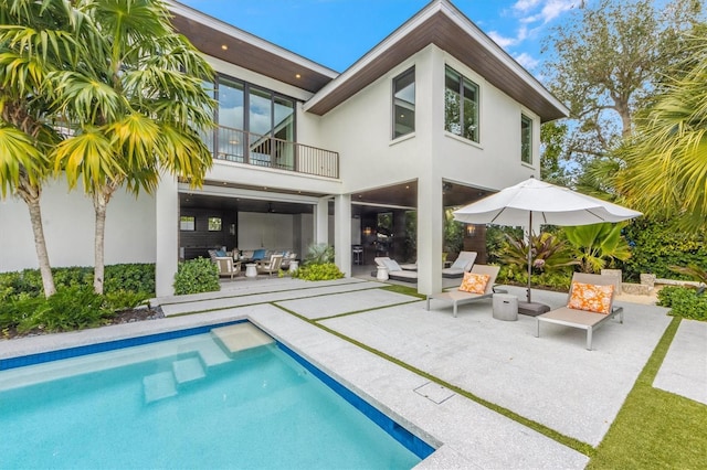 back of property featuring a patio area, stucco siding, an outdoor pool, and a balcony