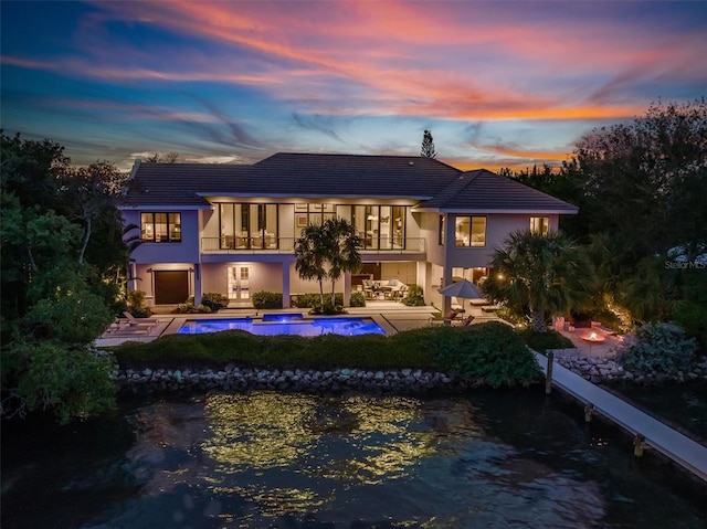 back of property at dusk with a balcony, a patio area, an outdoor pool, and stucco siding