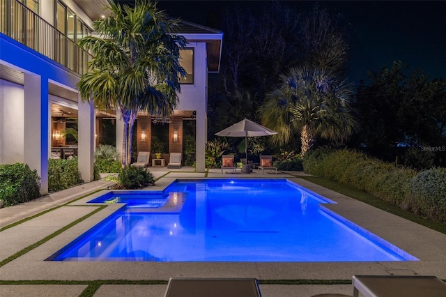 pool at twilight with a patio area and a pool with connected hot tub