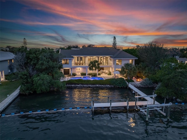 back of property at dusk featuring a water view, a tile roof, a patio, an outdoor pool, and boat lift