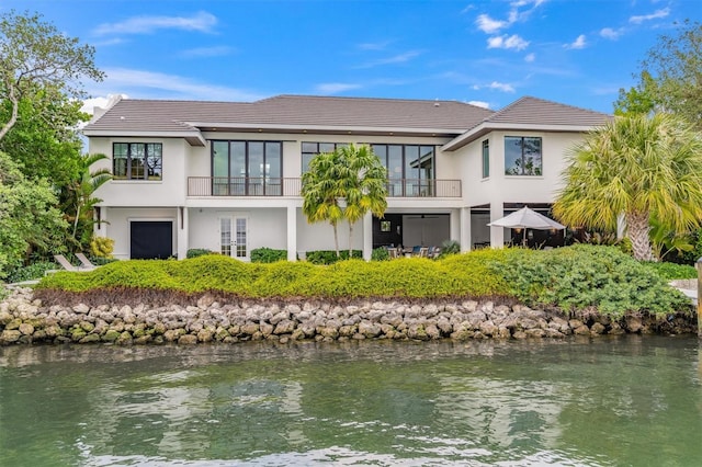 rear view of property with stucco siding, a water view, and a balcony