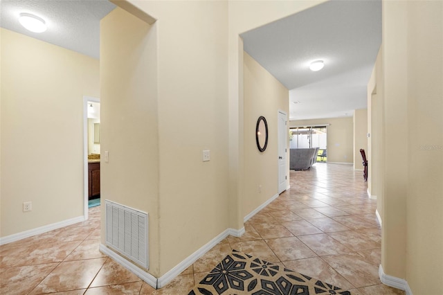 hall featuring light tile patterned floors, a textured ceiling, visible vents, and baseboards