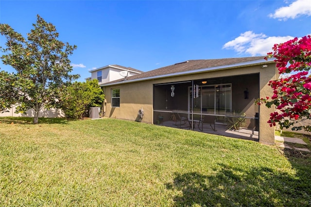 back of property featuring a sunroom, central AC, a yard, and stucco siding