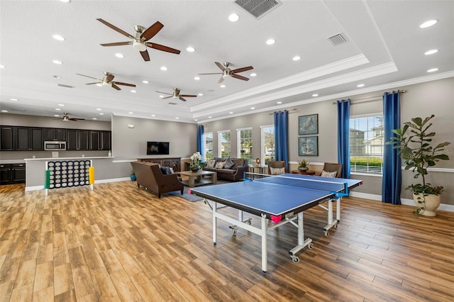 recreation room with light wood-style floors, visible vents, a tray ceiling, and ornamental molding