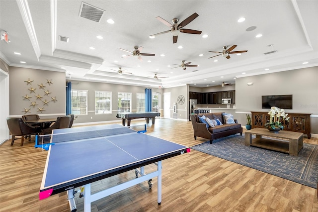 game room with light wood-type flooring, a raised ceiling, visible vents, and crown molding