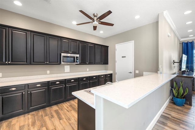 kitchen with dark cabinets, recessed lighting, stainless steel microwave, and light wood-style flooring