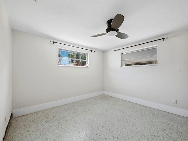 empty room with speckled floor, a ceiling fan, and baseboards