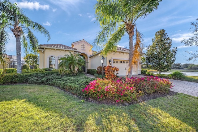 mediterranean / spanish house with a front yard, decorative driveway, an attached garage, and stucco siding