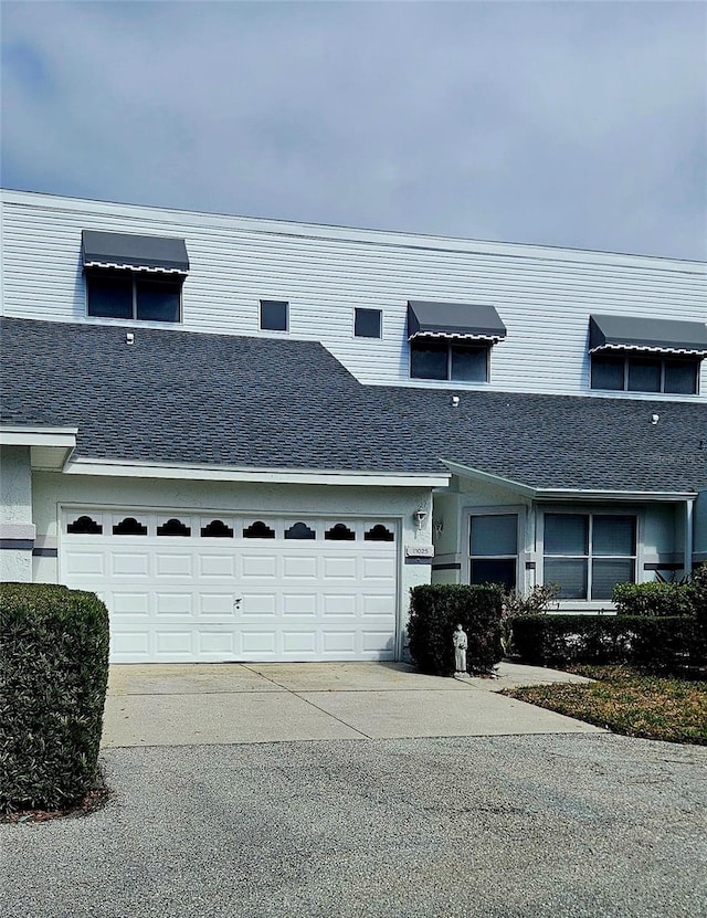 view of property featuring a garage, concrete driveway, a shingled roof, and stucco siding