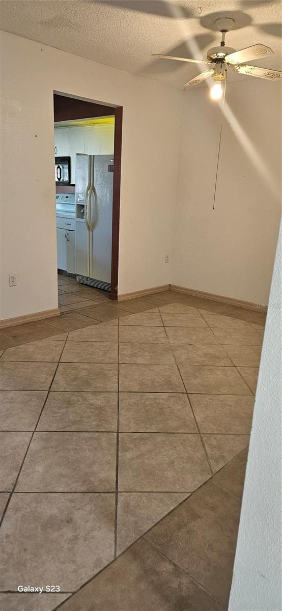 tiled spare room featuring a ceiling fan, a textured ceiling, and baseboards