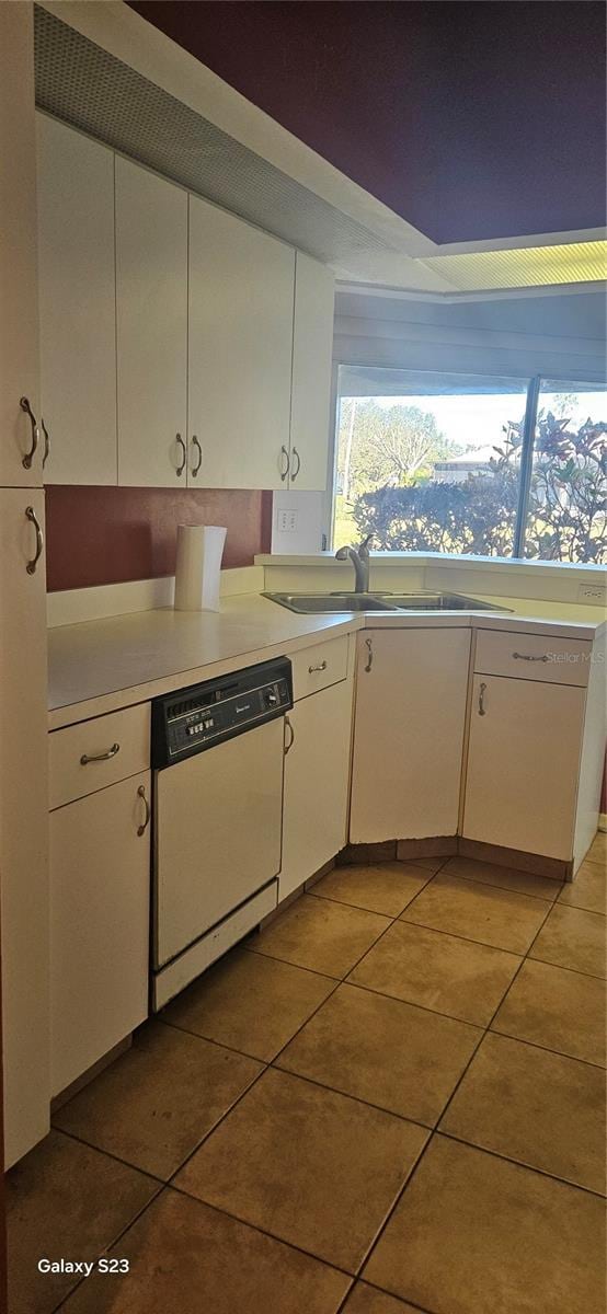 kitchen featuring light tile patterned floors, a sink, white cabinetry, light countertops, and dishwasher