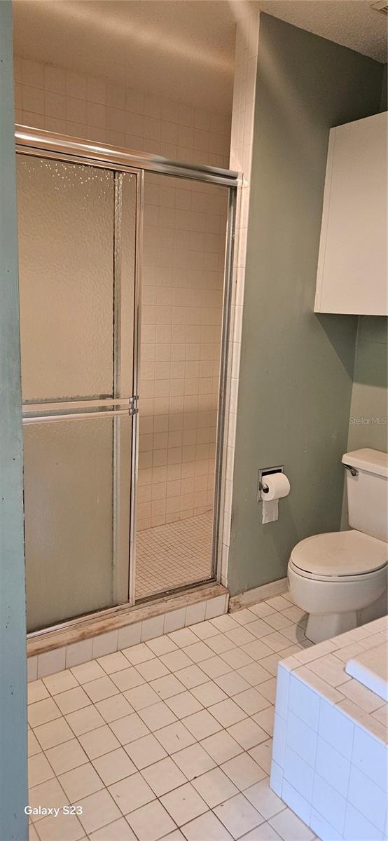 bathroom featuring toilet, a shower stall, a textured ceiling, and tile patterned flooring