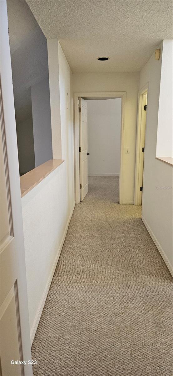 corridor featuring light carpet, a textured ceiling, and baseboards