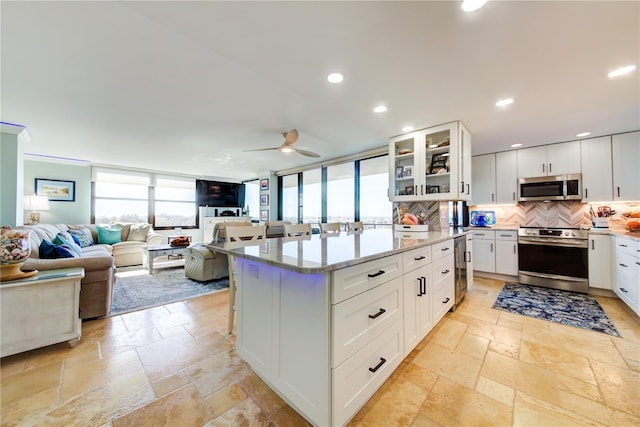 kitchen featuring white cabinets, stone tile floors, stainless steel appliances, and decorative backsplash