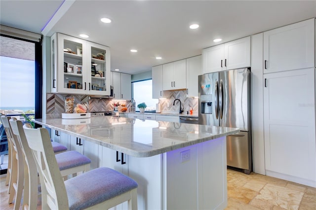 kitchen with light stone countertops, white cabinetry, glass insert cabinets, and stainless steel appliances