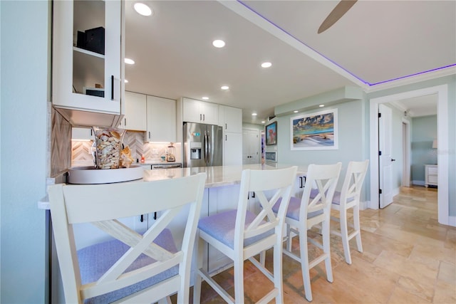 kitchen with recessed lighting, a breakfast bar, white cabinets, stainless steel refrigerator with ice dispenser, and decorative backsplash