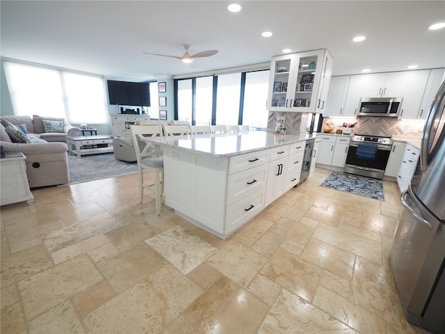 kitchen with a breakfast bar, stainless steel appliances, stone tile flooring, decorative backsplash, and open floor plan