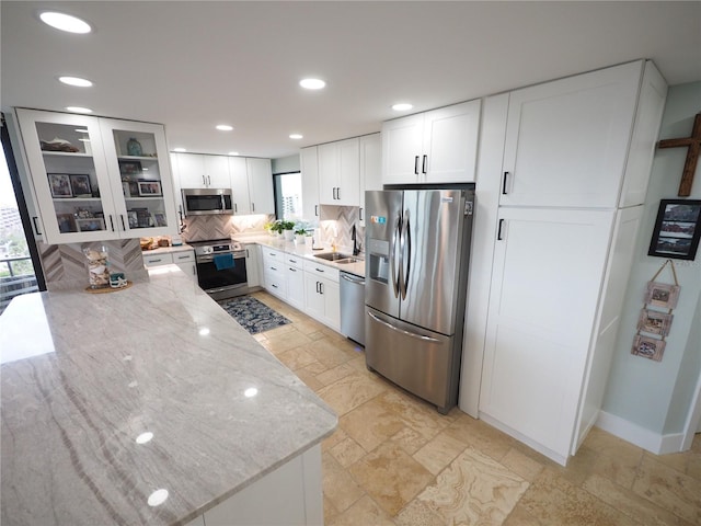 kitchen featuring appliances with stainless steel finishes, white cabinets, a sink, and light stone counters