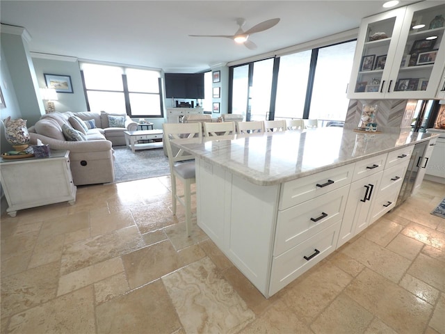 kitchen with stone tile floors, a breakfast bar, white cabinets, light stone countertops, and glass insert cabinets