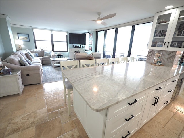 kitchen with light stone counters, a breakfast bar, stone tile flooring, glass insert cabinets, and white cabinets