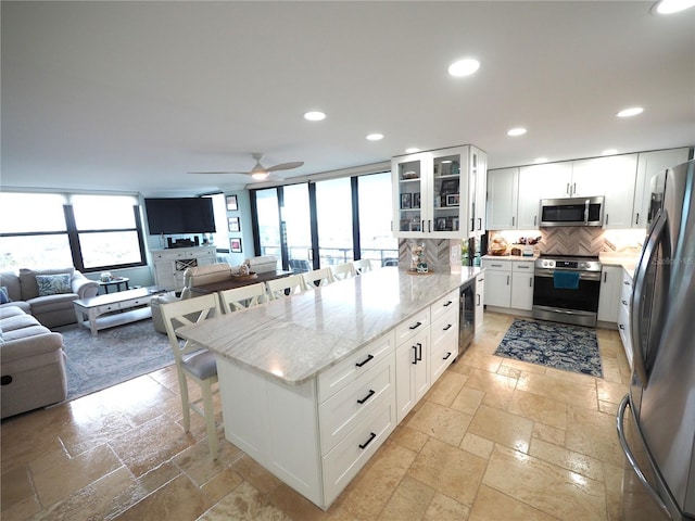 kitchen featuring a breakfast bar area, recessed lighting, stone tile flooring, backsplash, and appliances with stainless steel finishes