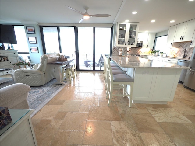 kitchen with backsplash, glass insert cabinets, white cabinets, light stone countertops, and a kitchen bar