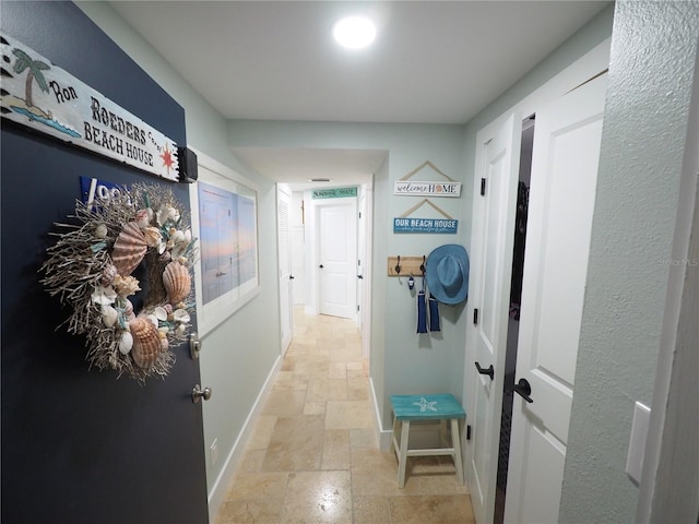 hallway with stone tile floors and baseboards