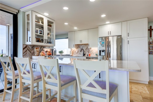 kitchen featuring a kitchen bar, stone tile flooring, glass insert cabinets, white cabinets, and stainless steel fridge with ice dispenser