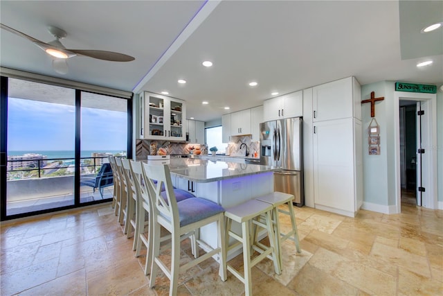 kitchen with a center island, stone tile floors, tasteful backsplash, glass insert cabinets, and stainless steel fridge with ice dispenser