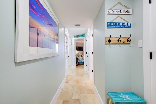 hall featuring baseboards, visible vents, and stone tile floors