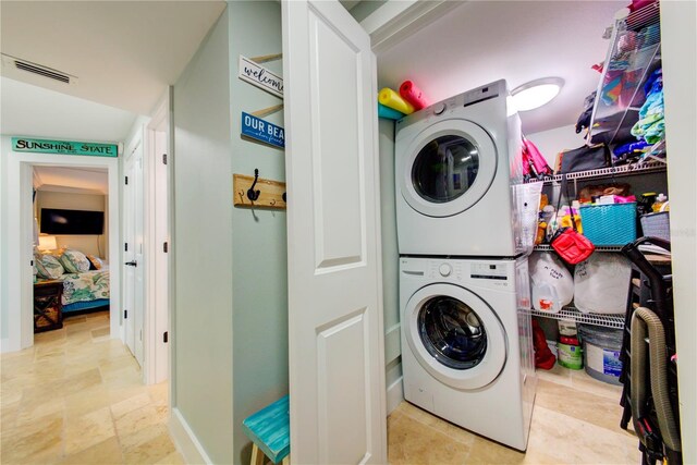 clothes washing area with laundry area, visible vents, and stacked washing maching and dryer