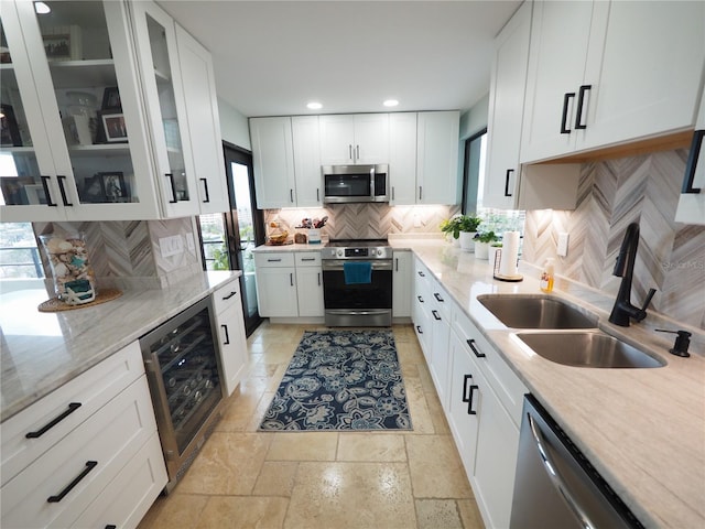 kitchen featuring beverage cooler, a sink, white cabinetry, appliances with stainless steel finishes, and light stone countertops